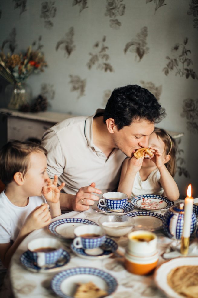 Pai comendo na mesa,junto aos seus dois filhos.