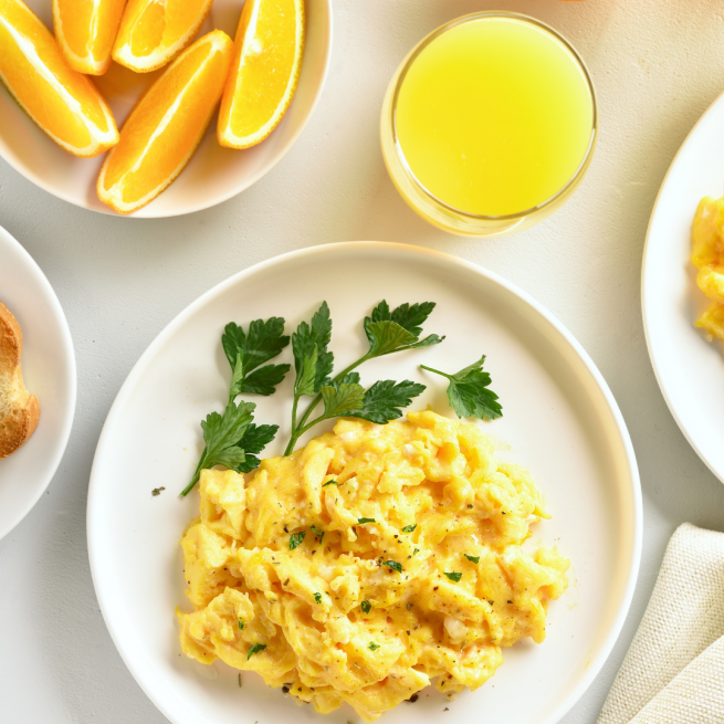 Prato com ovo mexido, e um copo de suco natural de laranja.