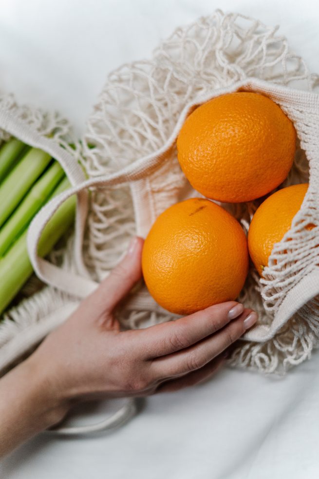 Pessoa pegando da sacola branca, uma laranja da variedade bahia.