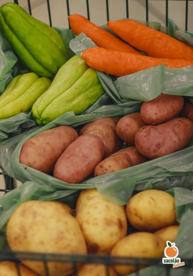 Sacolas de compras com os seguintes itens: batatas inglesas, batatas asterix, chuchus, e cenouras.