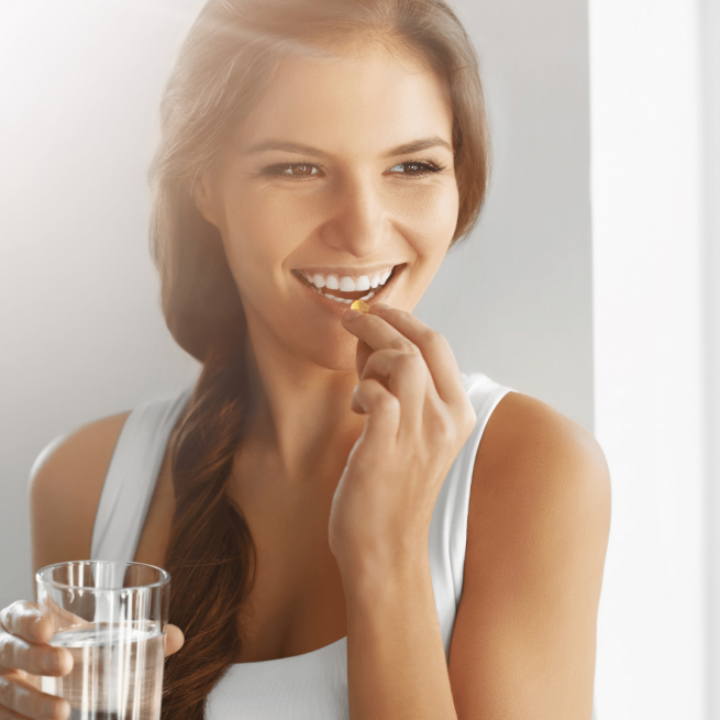 Mulher tomando vitaminas e suplementos, que ajudam no fortalecimento do sistema imunológico.